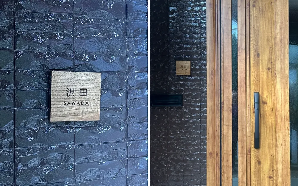 ブラック系の壁に木製の表札を付けている家。